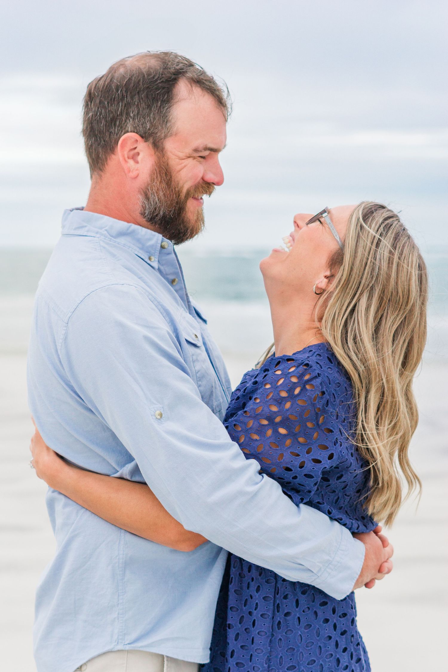 A couple laughs together during an intimate moment on a cloudy beach.