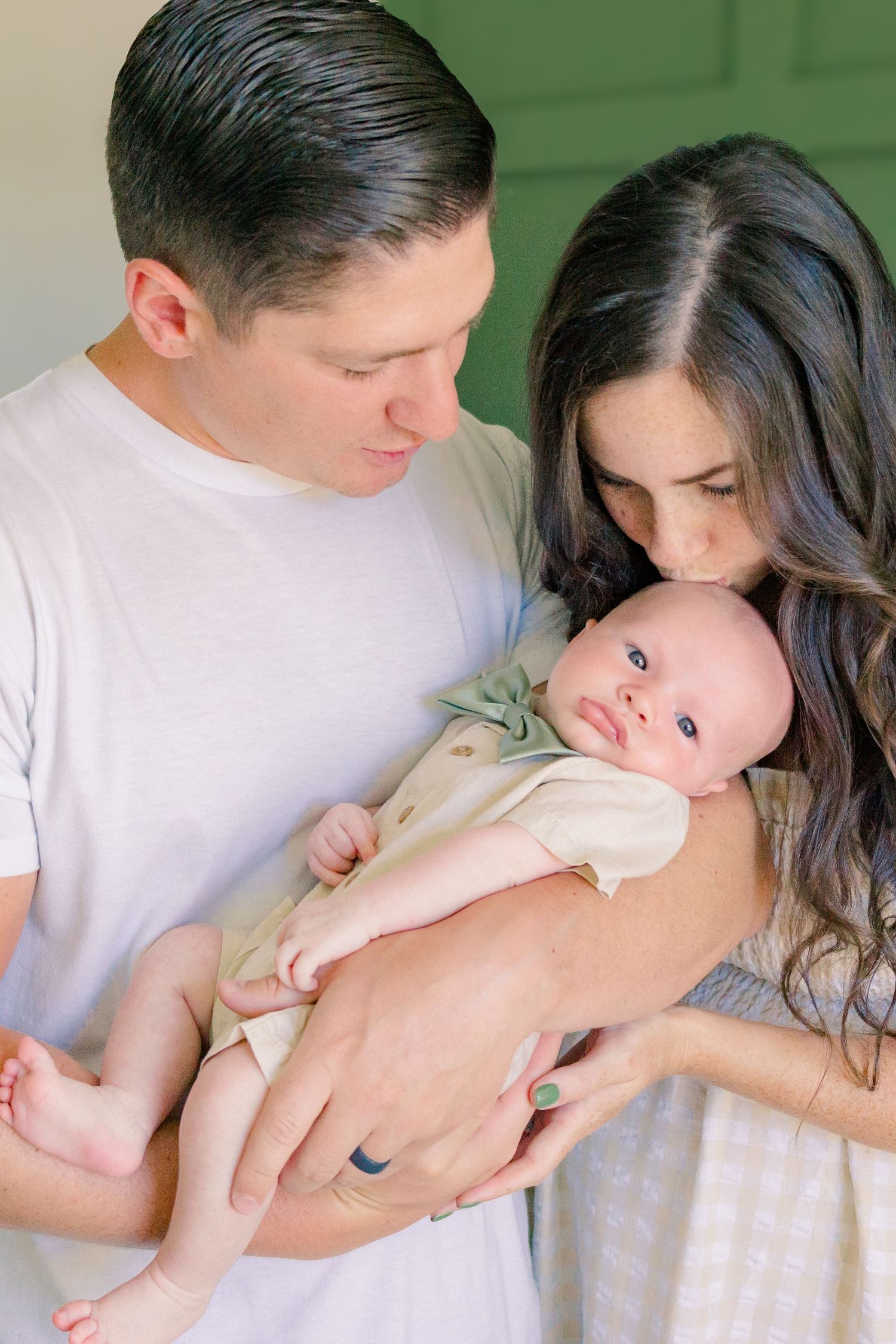 Tender moment as parents hold and gaze at their newborn baby against green wall background.