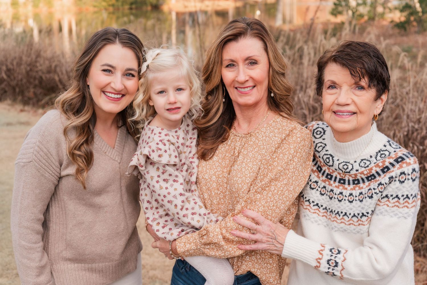Multi-generational portrait of four people in cozy sweaters against an autumn background.