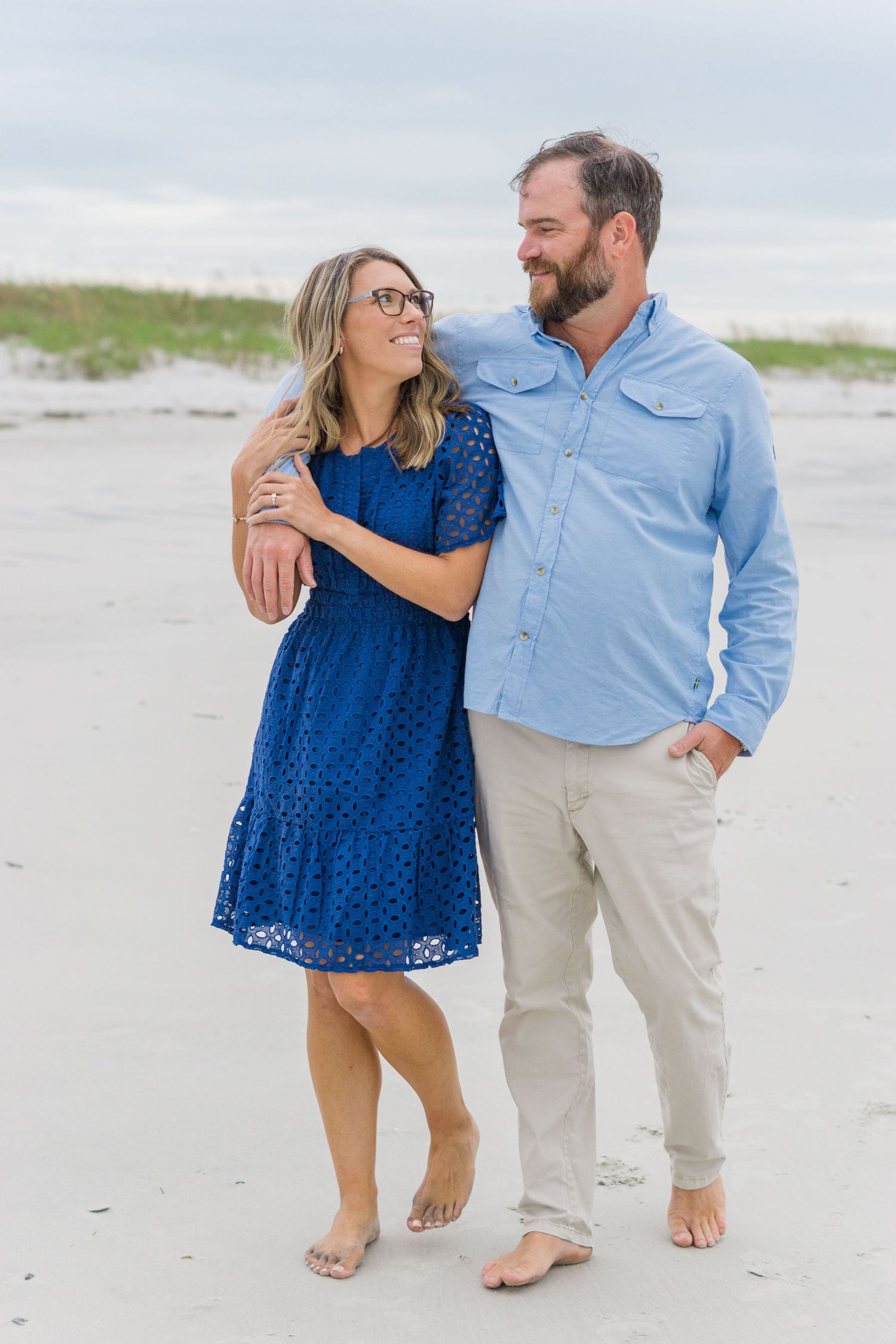 A couple takes a romantic beach walk together wearing casual coastal attire.