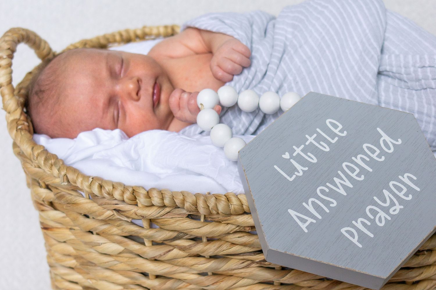 Sleeping newborn in wicker basket with gray sign and pom pom decorations.