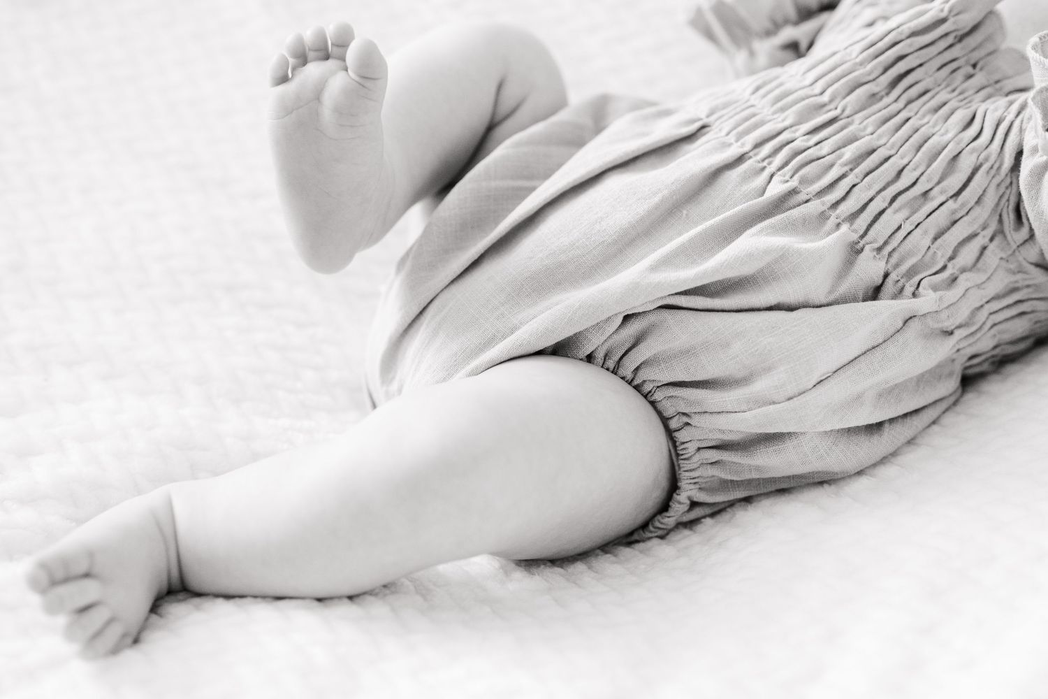 Black and white close-up photograph of baby feet and ruffled clothing against white background.