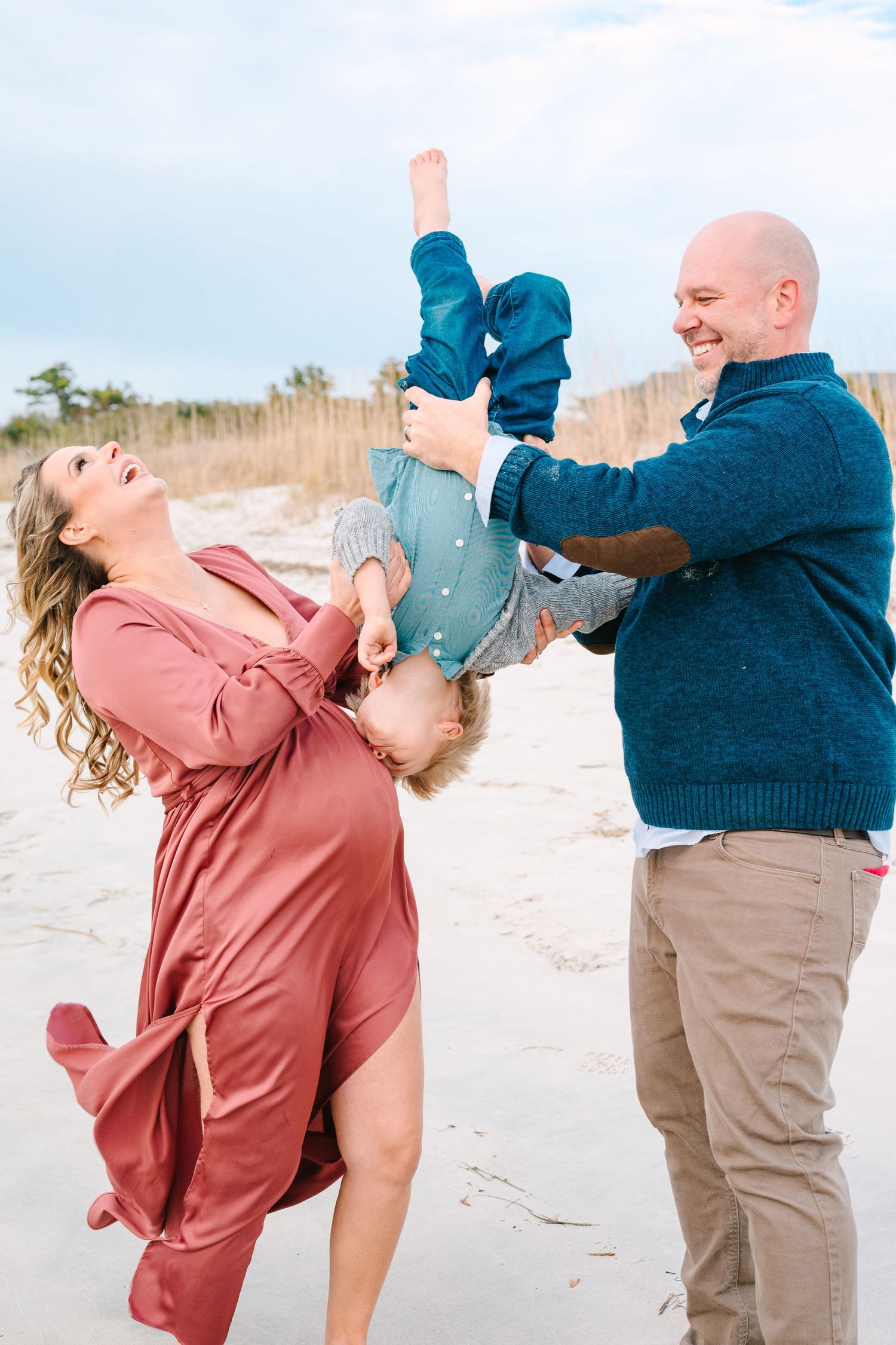 Family plays and laughs together during a joyful moment on the beach on a bright sunny day.