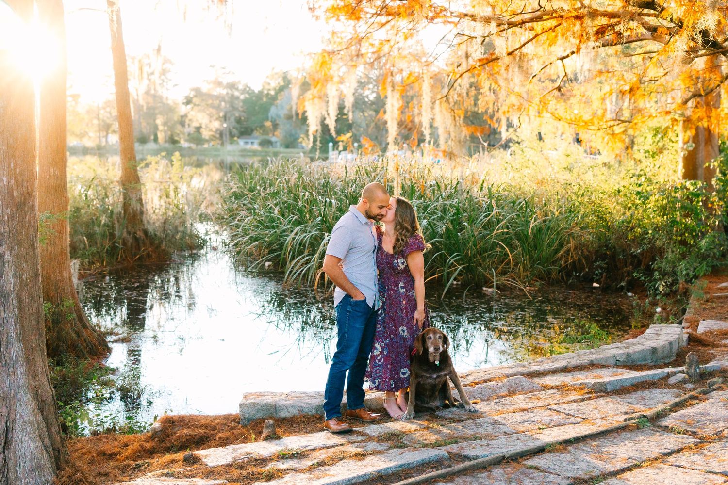 Intimate couple moment captured during sunset by waterfront with fall foliage.