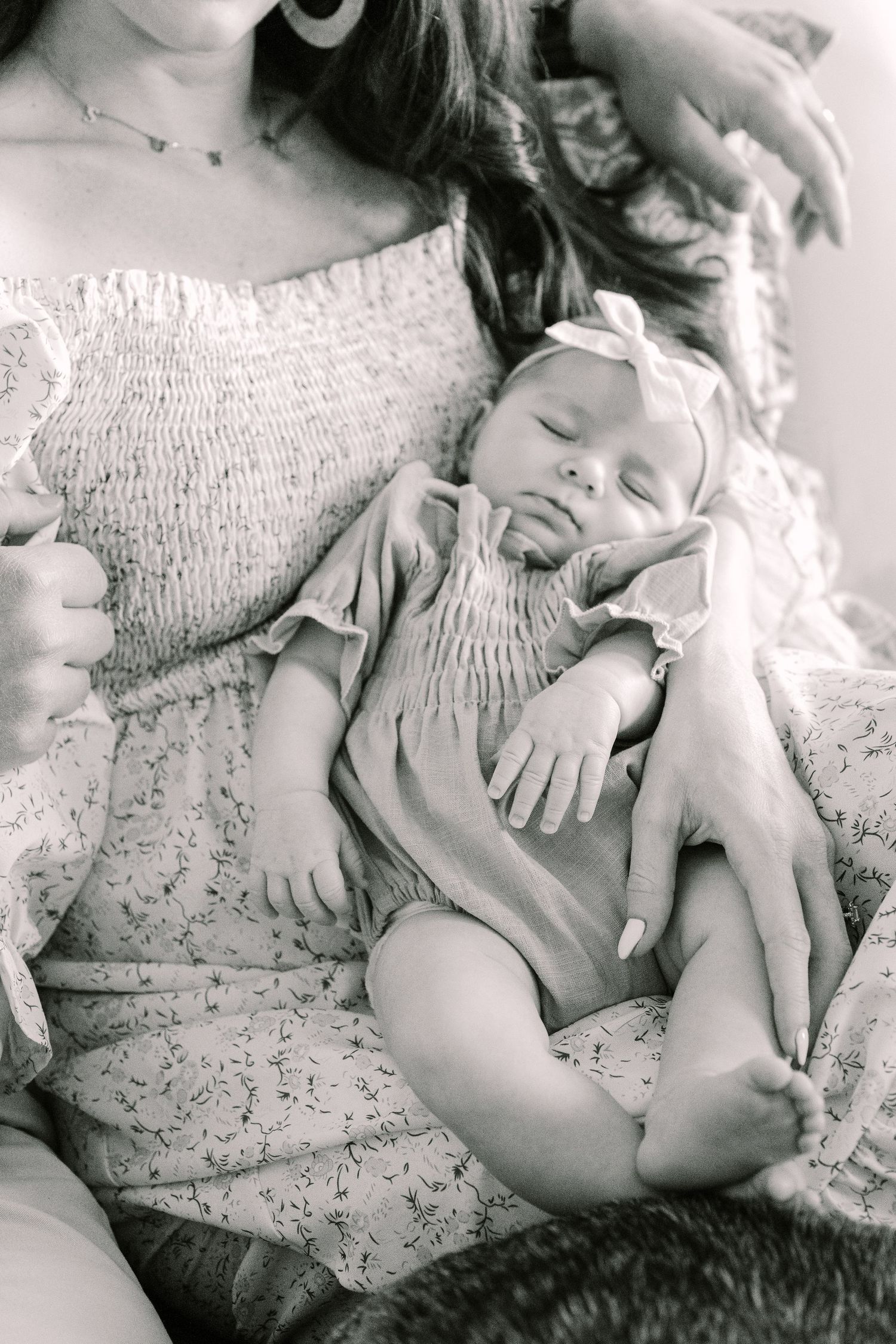 A black and white portrait of a sleeping infant wearing a smocked dress resting peacefully on someone's lap.