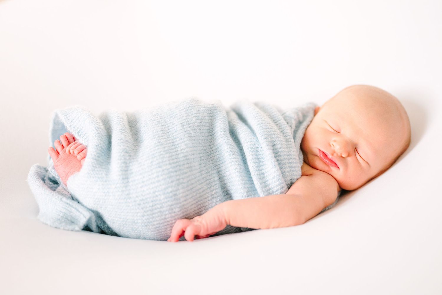 A sleeping baby wearing a soft blue onesie lies peacefully on a white background.