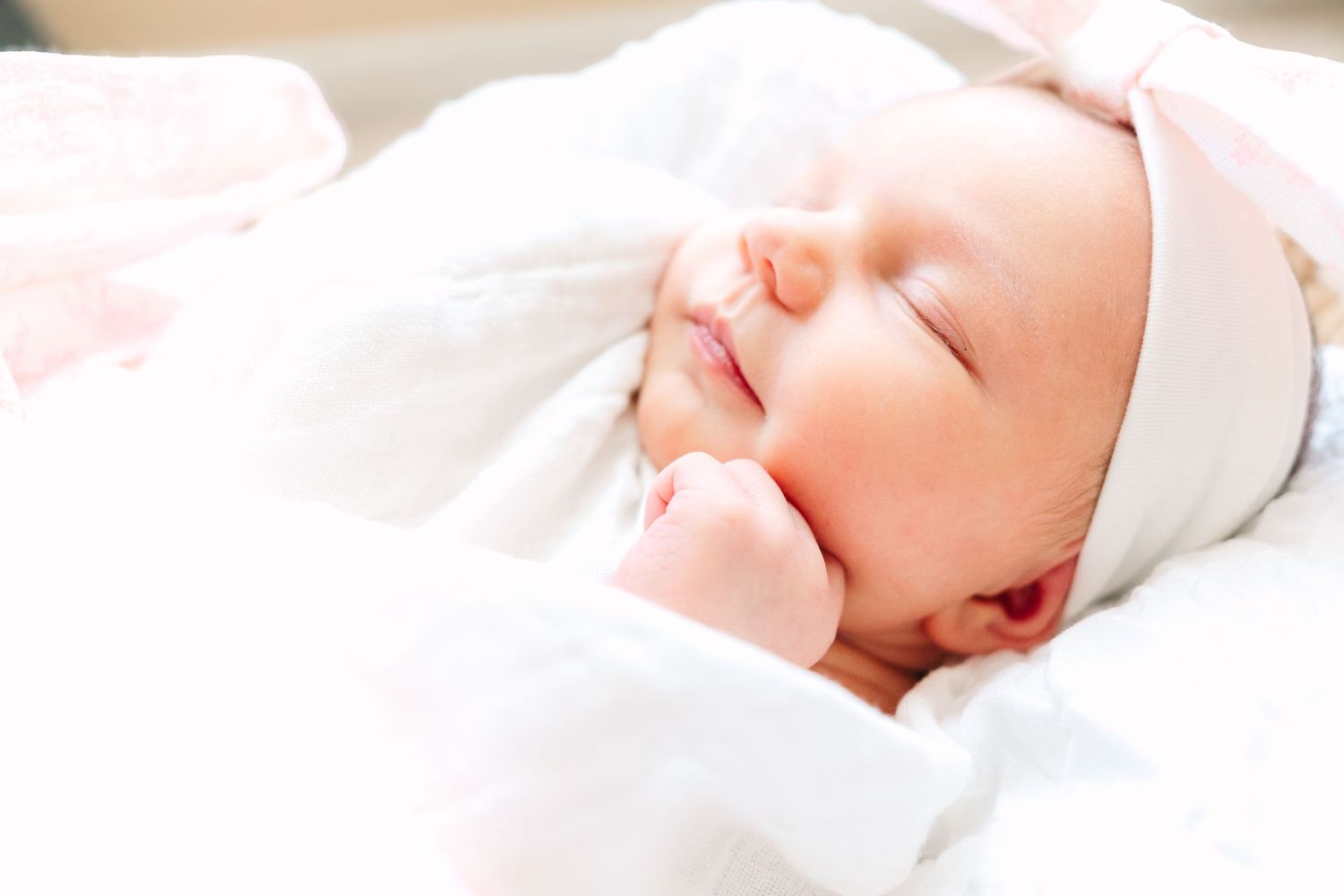 A sleeping newborn wearing white wrapped in cozy blankets with soft lighting.