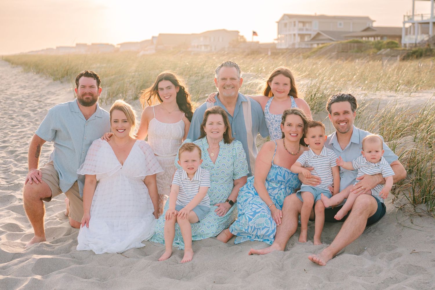 Extended family gathered on beach sand during sunset for group photo.