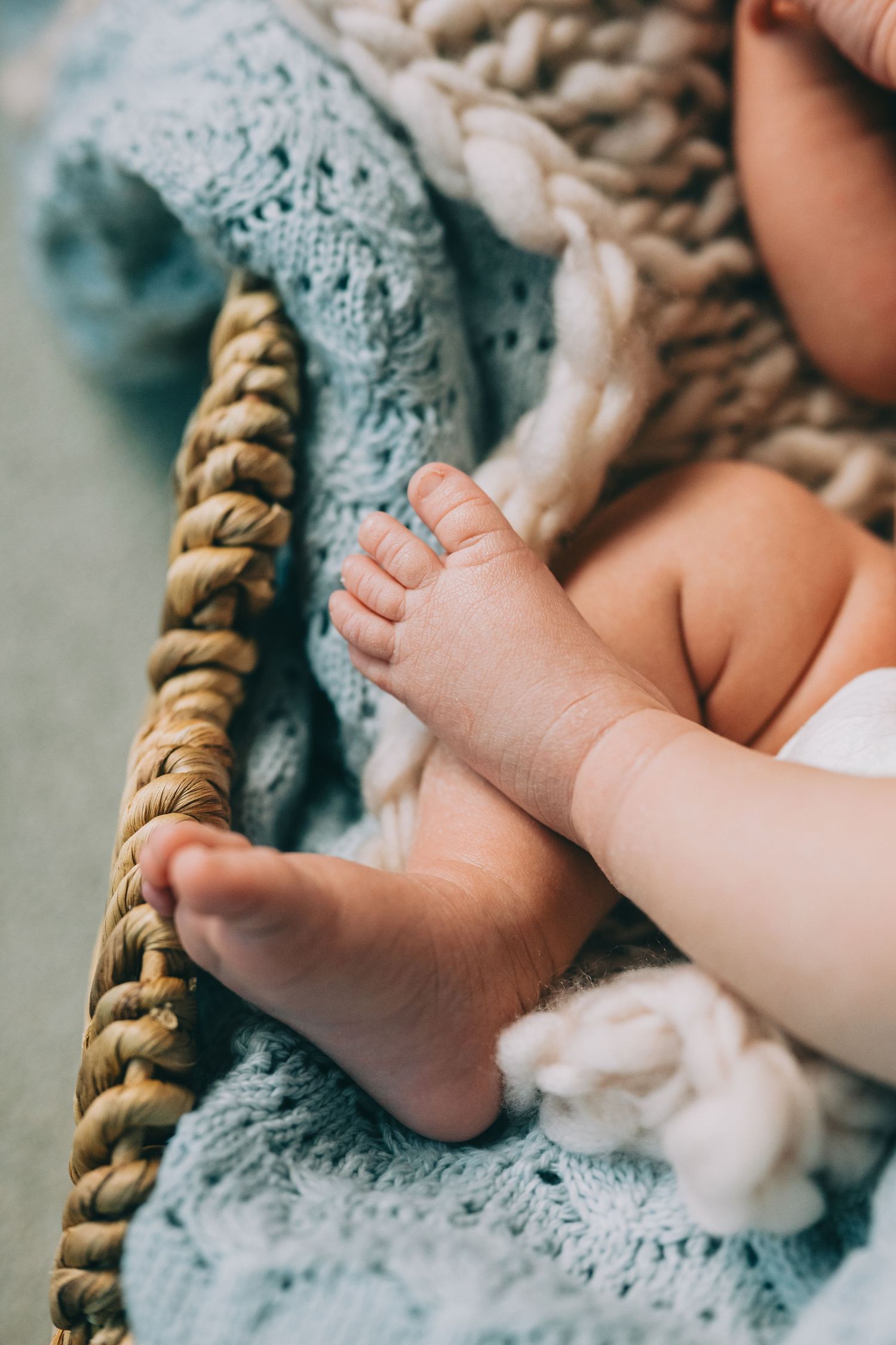 Close-up of tiny baby feet resting on soft blue knitted blanket with woven basket details.