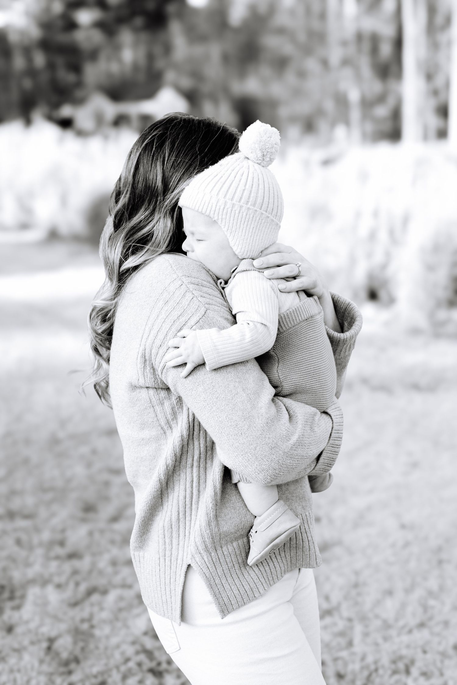 Person in sweater holding baby in white knit outfit in black and white photo.