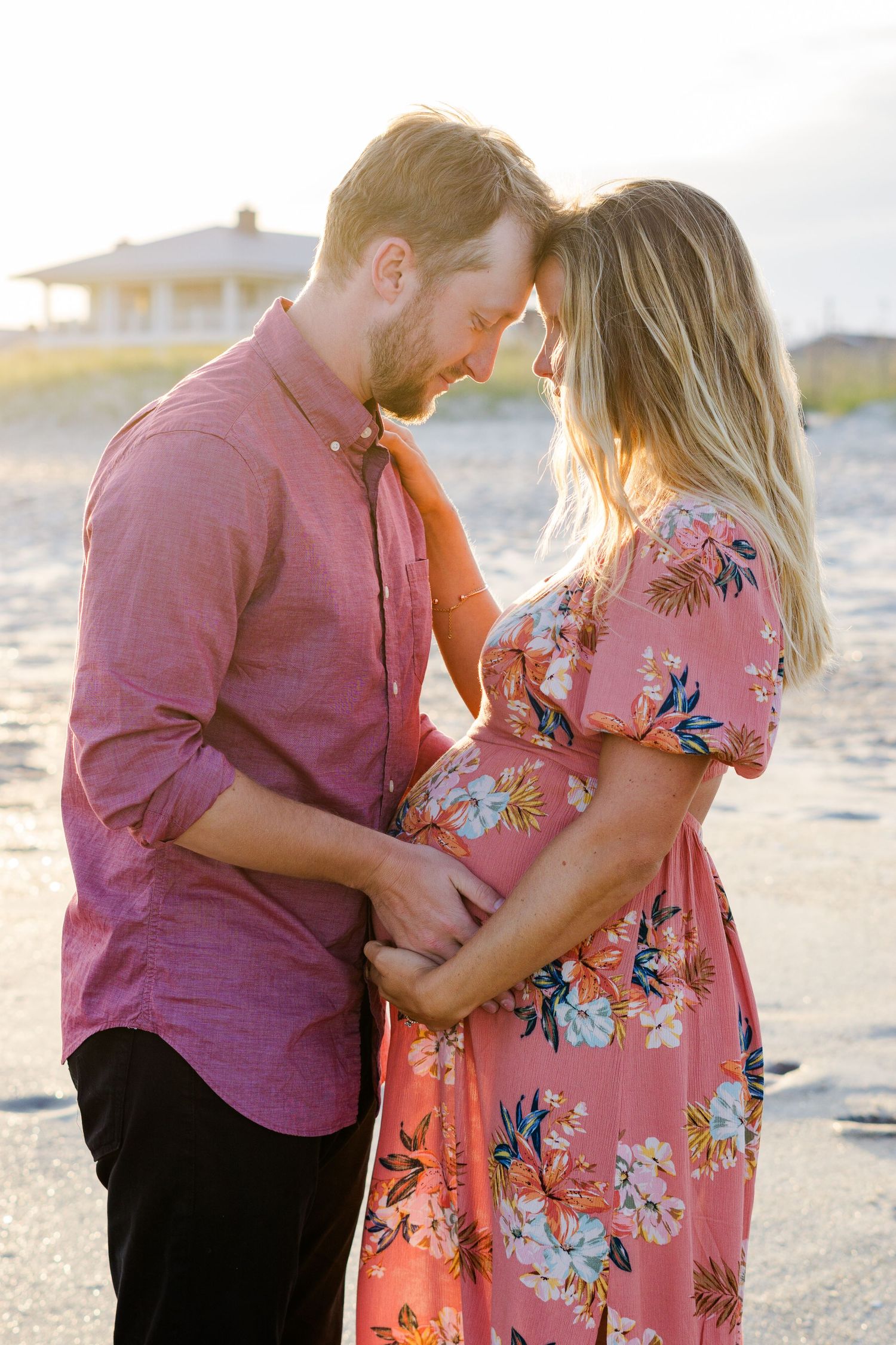 Intimate forehead touch moment between couple during beach maternity photoshoot at sunset.