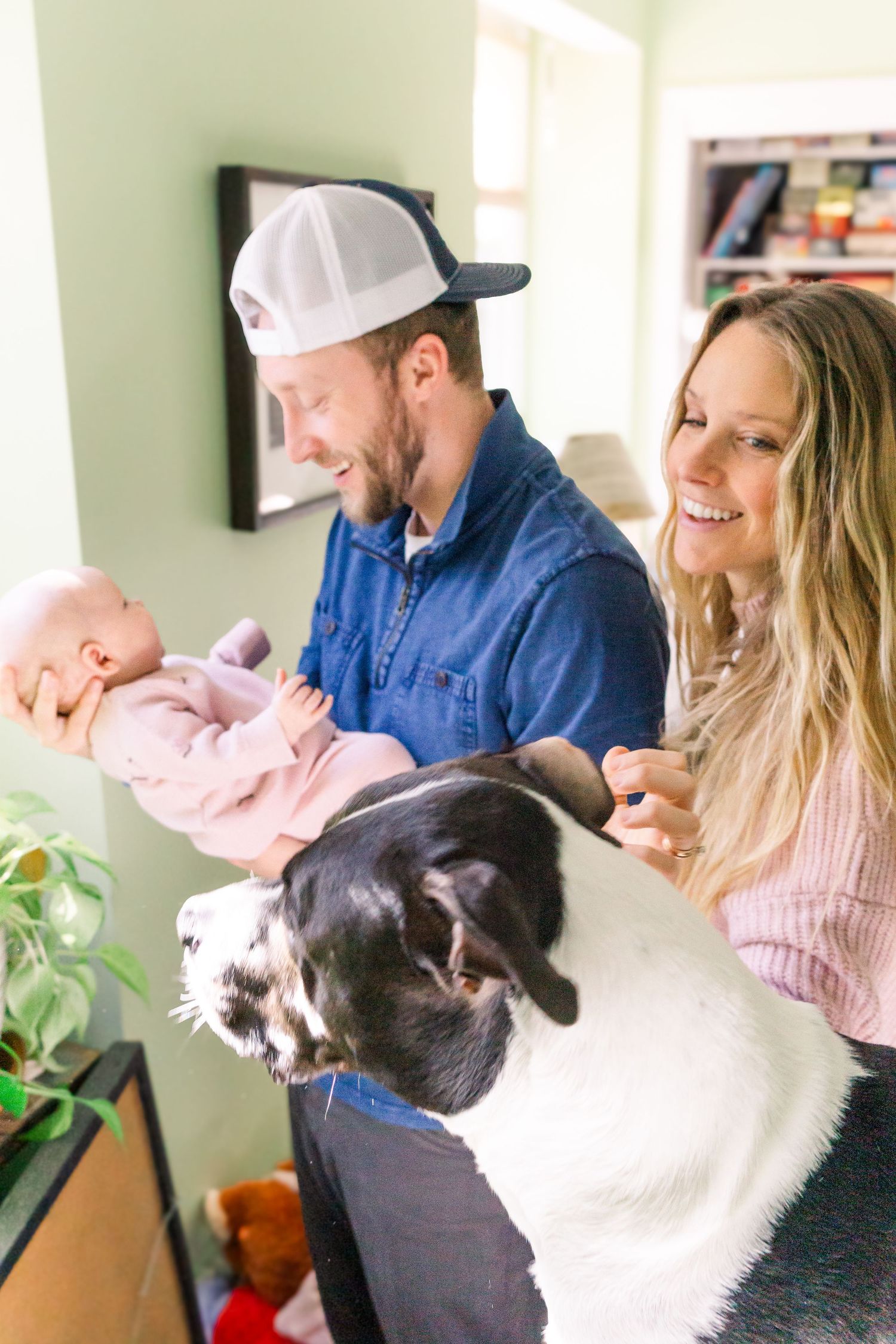 A family moment at home with their baby and large black and white dog on the couch.