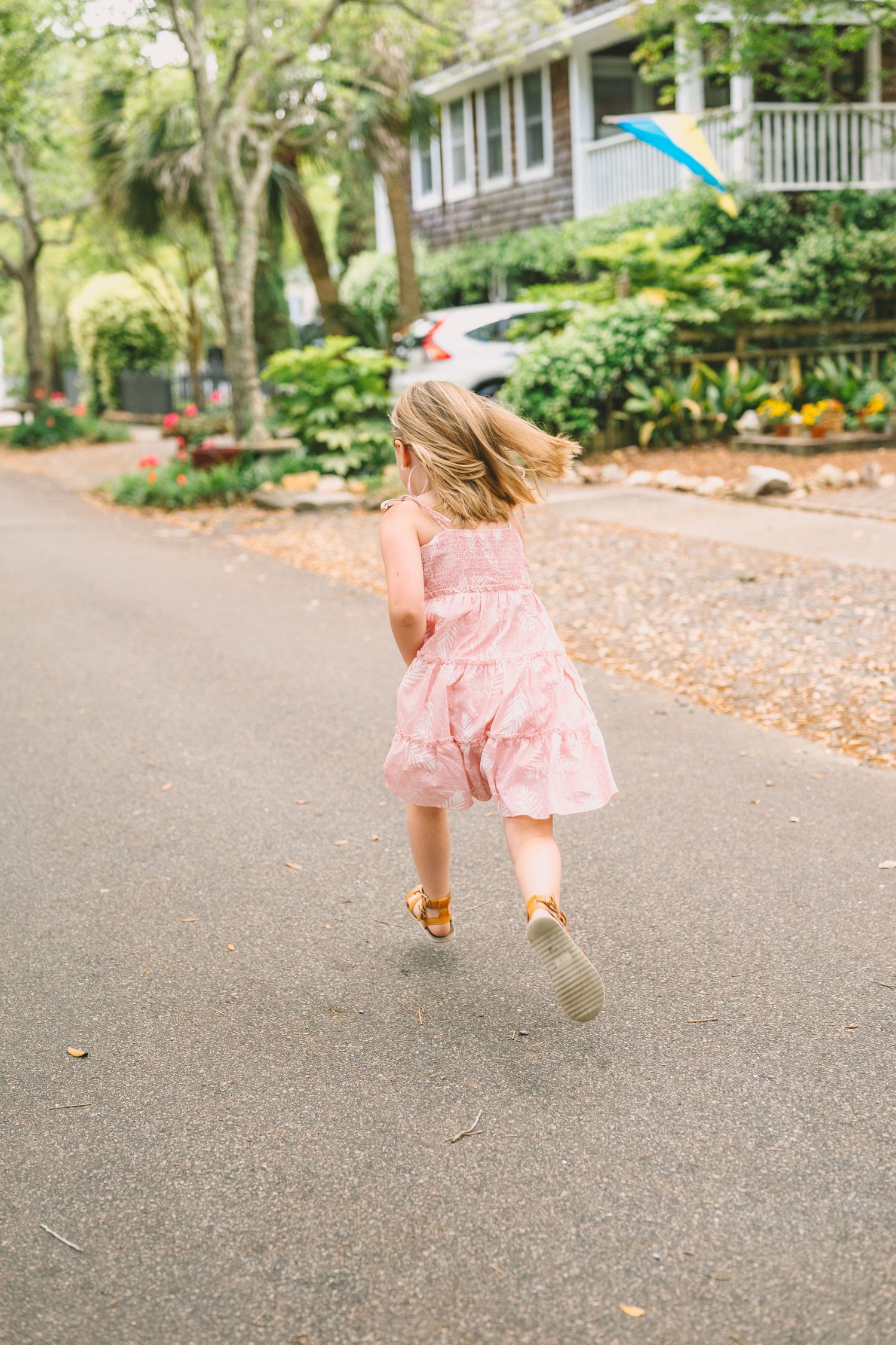 Young child in a pink dress skips joyfully down a residential street lined with trees.
