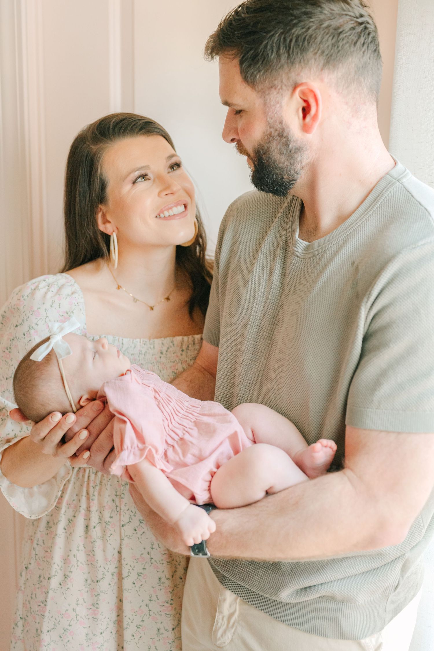 A couple lovingly holds their newborn baby dressed in pink, sharing a tender moment together.