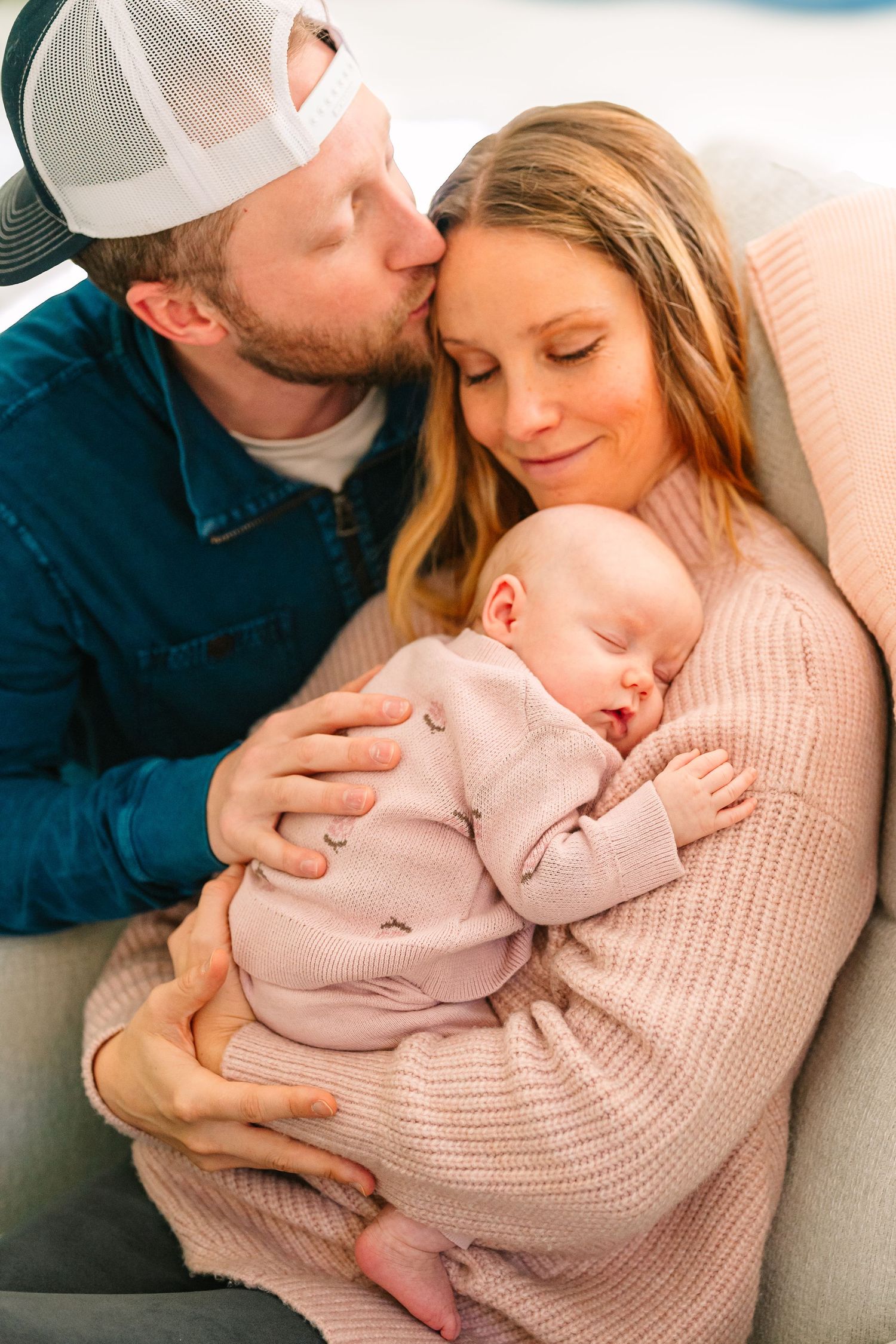A peaceful family moment as parents snuggle with their sleeping infant on a couch.