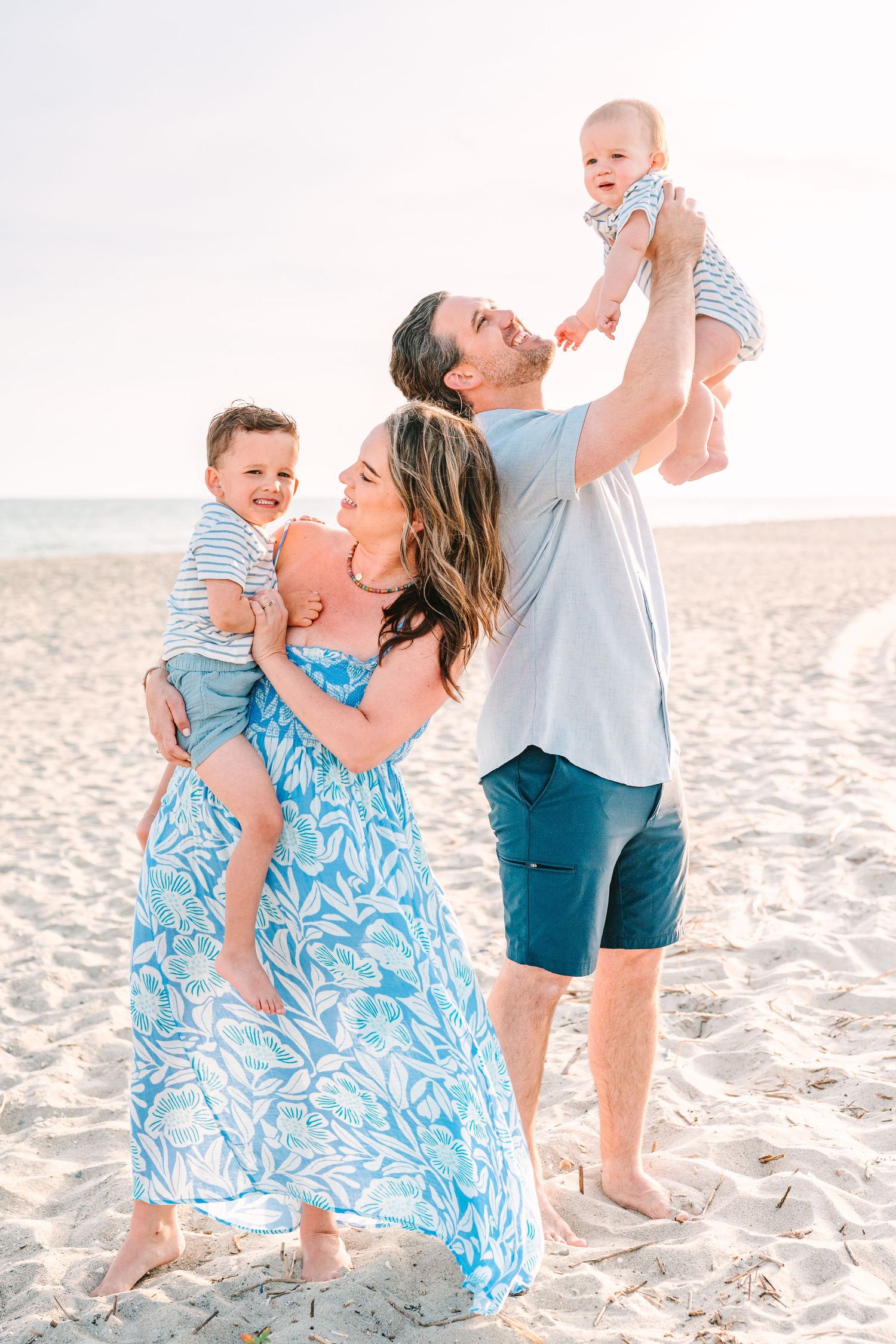 Happy parents playing with small children on beach wearing coordinated blue and white outfits.