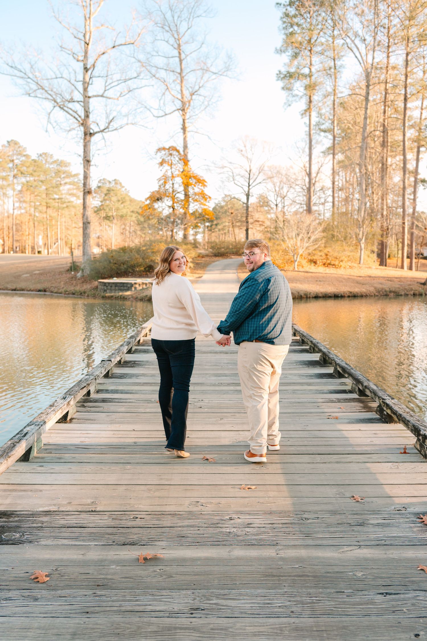 A couple stands together on a wooden dock overlooking a serene lake at sunset.