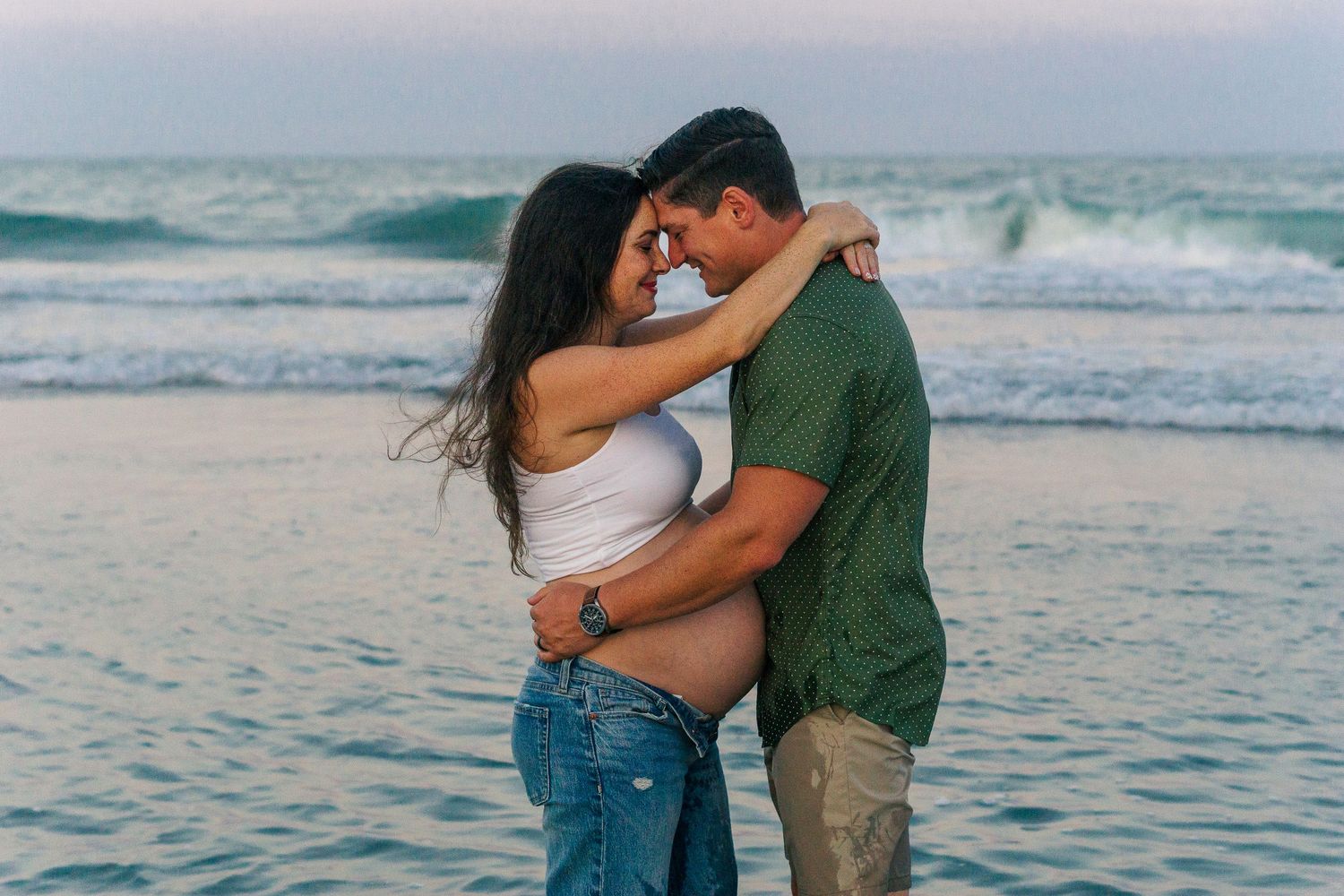 Romantic couple embracing on a beach at sunset with ocean waves in the background.