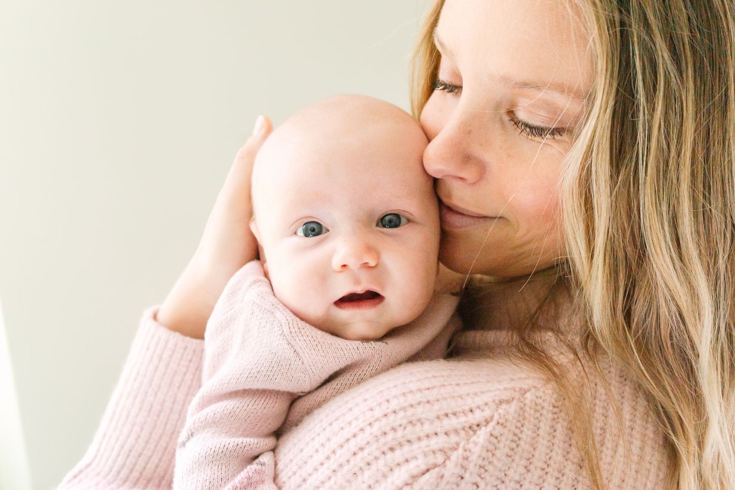 A tender moment shared between parent and infant wearing matching soft pink sweaters against a light background.
