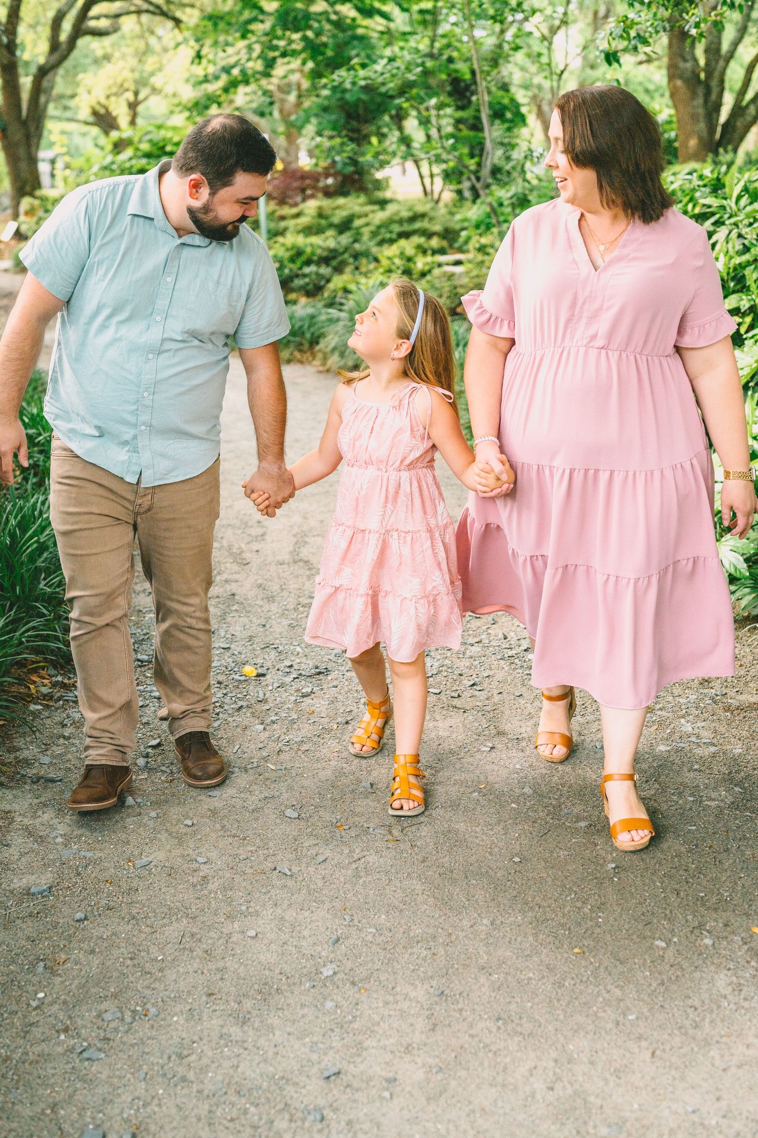 A family walks together on a tree-lined path wearing coordinated pink and blue outfits.