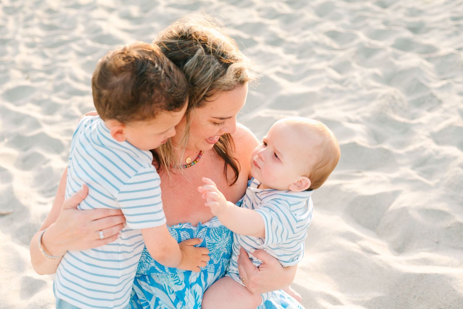 Parent shares joyful moment with children on sandy beach during sunset photo session.