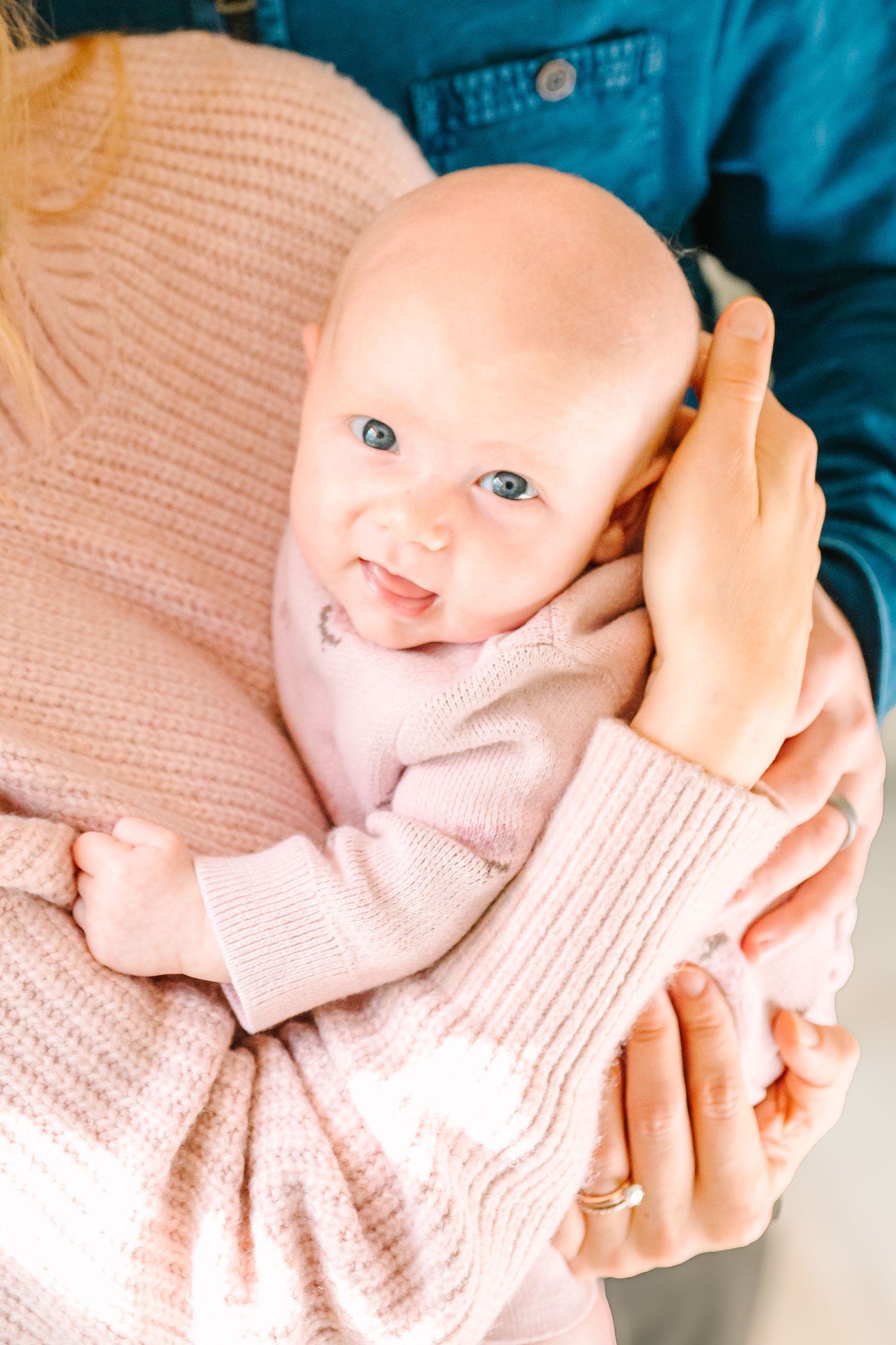 Sweet baby in soft pink knit sweater smiling and being held close in gentle embrace.