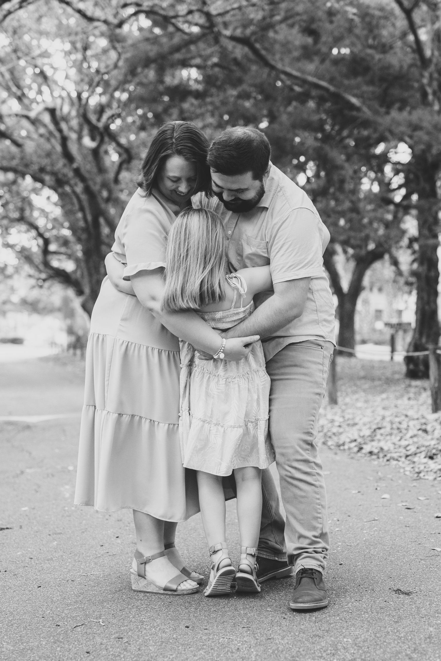 A tender black and white family moment captured outdoors in a park setting.