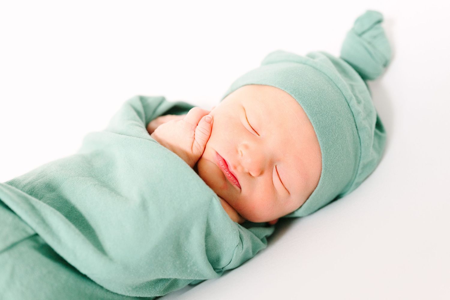 Peaceful sleeping newborn baby wearing mint green outfit and hat on white background.