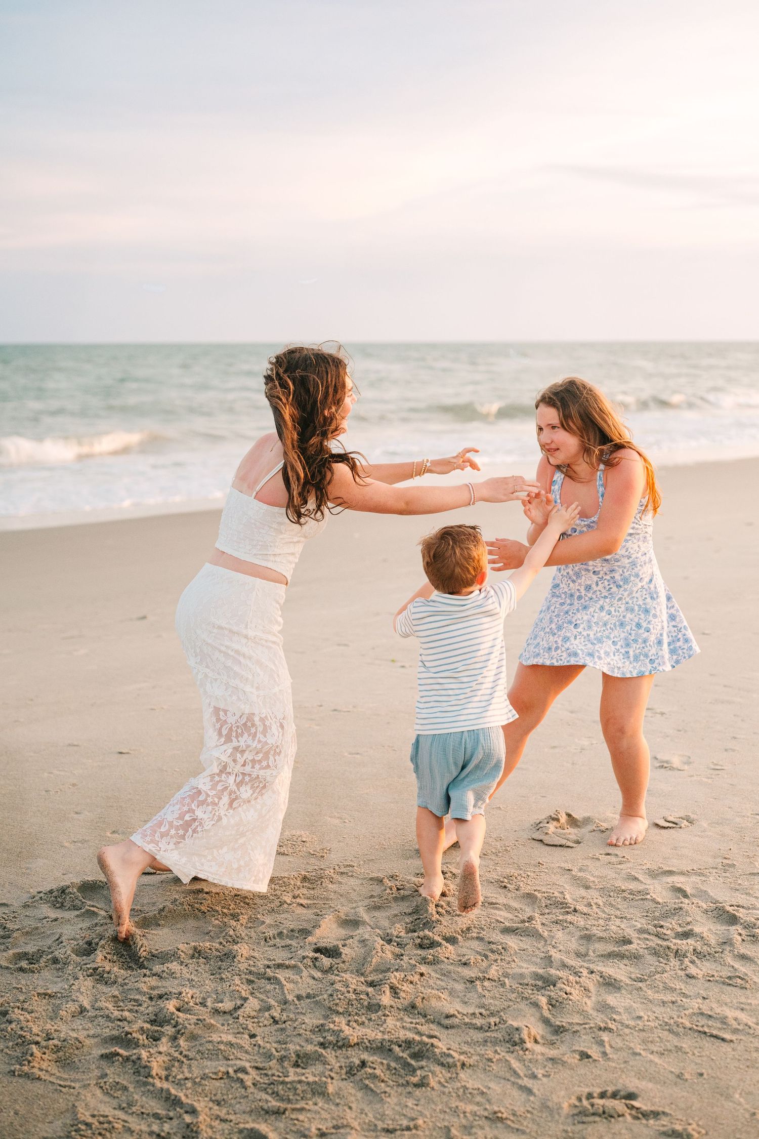 Three people dancing and playing together on beach during sunset photo session.