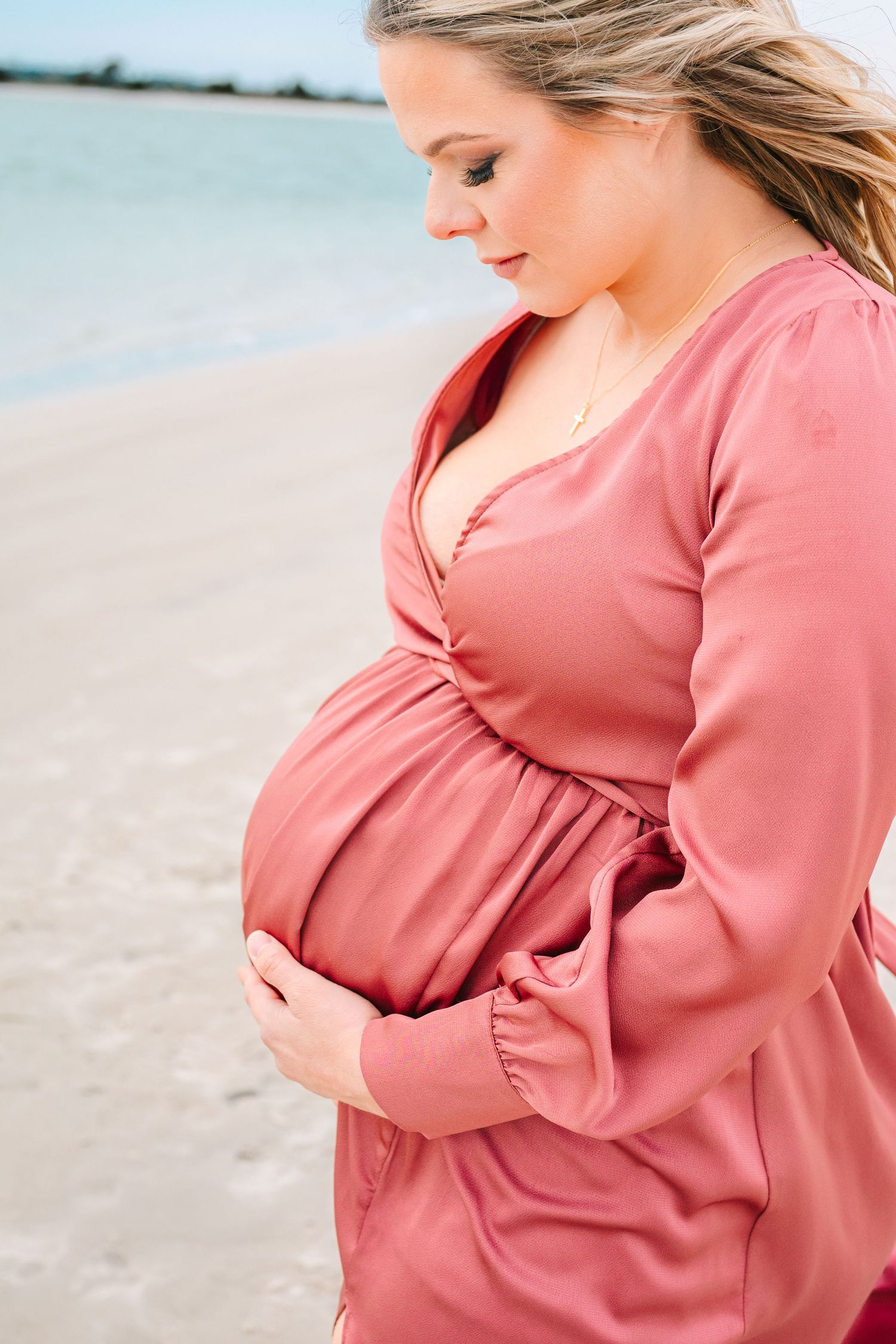 Maternity portrait featuring a coral dress against a beach backdrop.