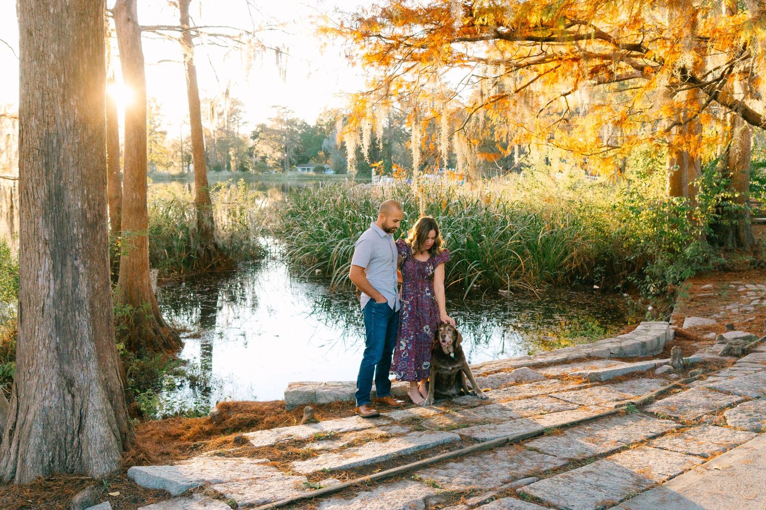 Couple stands on wooden walkway surrounded by autumn cypress trees and tranquil water.
