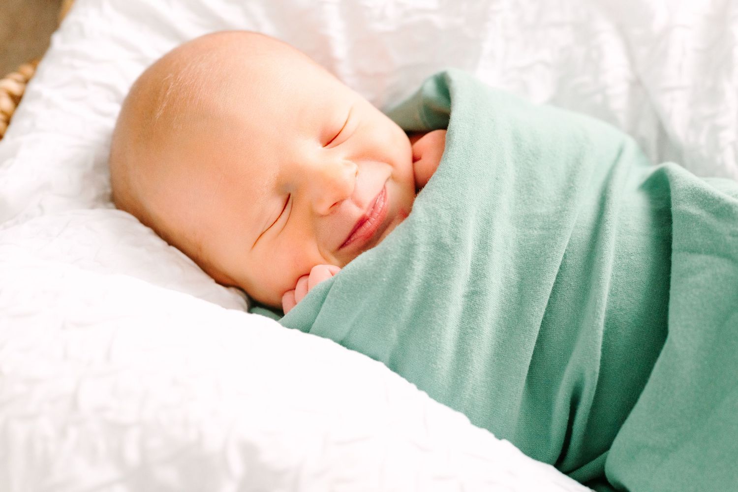 Newborn wrapped in mint green blanket sleeping on white cushioning.