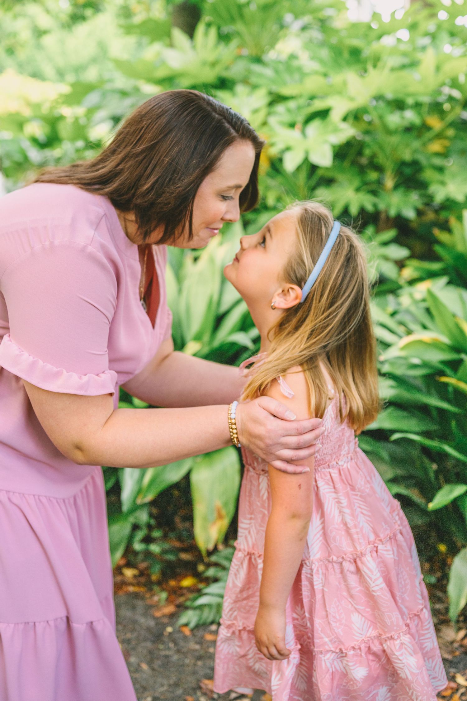 Two people in pink dresses share a tender moment while standing together in a garden setting.