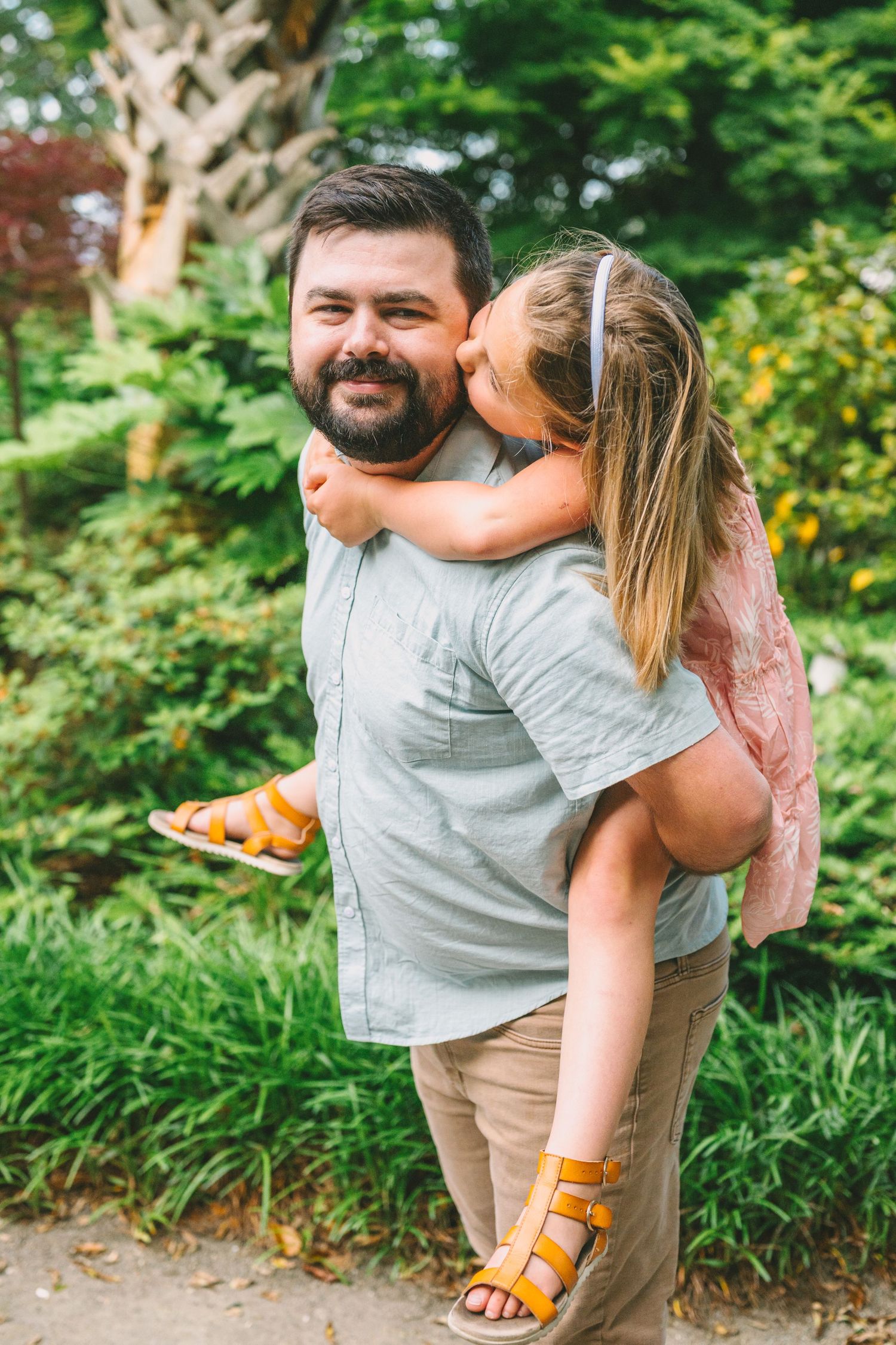A couple sharing a playful piggyback ride moment in a lush garden setting on a sunny day.