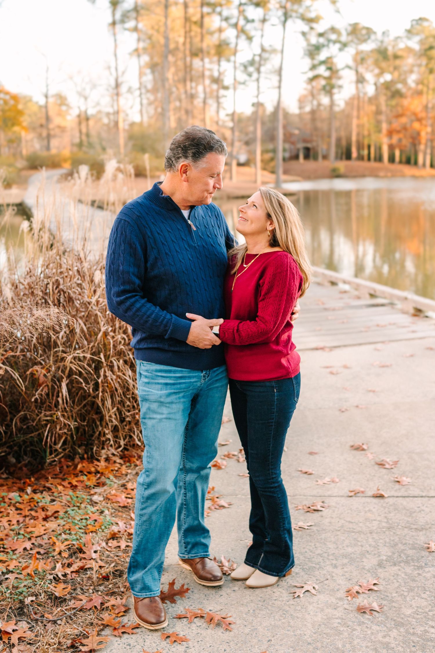 A couple embraces by a lake with autumn foliage in the background.