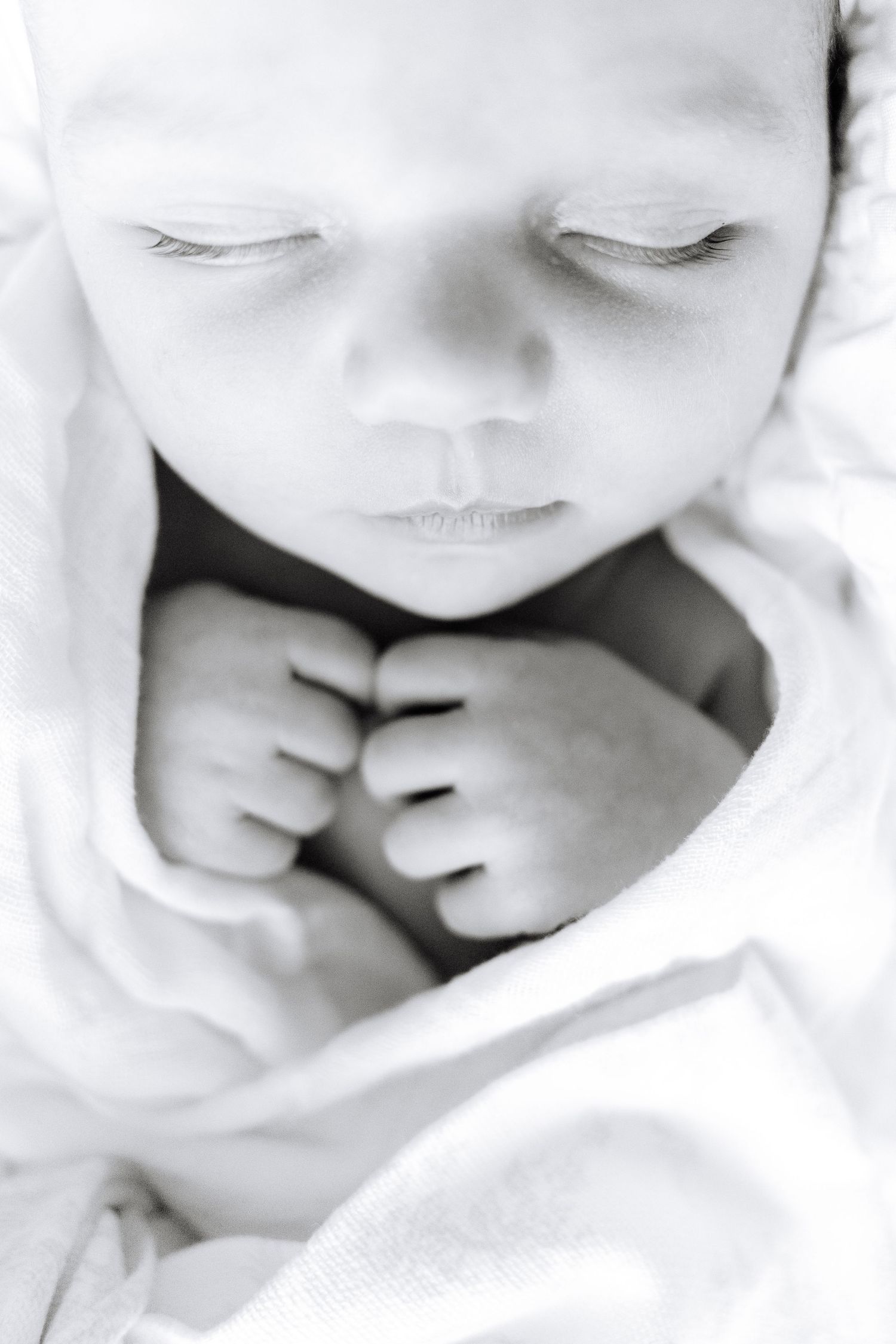 A sleeping newborn wrapped in soft pink and white blankets with delicate features.