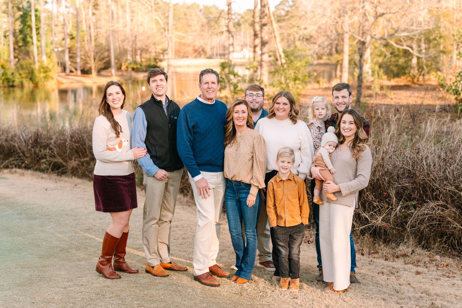 Family group portrait outdoors with autumn trees and natural scenery in the background.