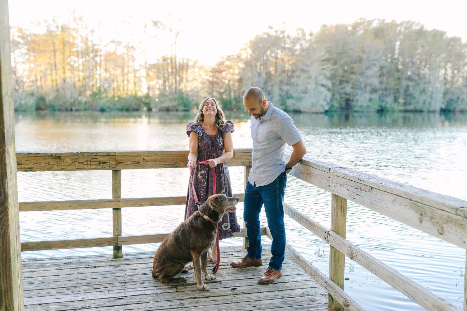 Family portrait with dog on wooden pier during golden hour by the lake.