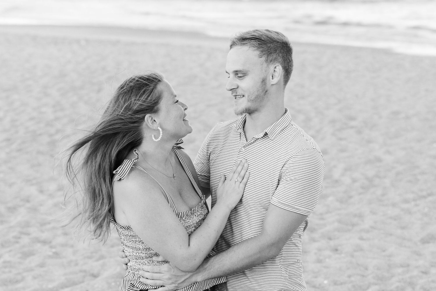 A joyful couple embraces and laughs together on a sandy beach.