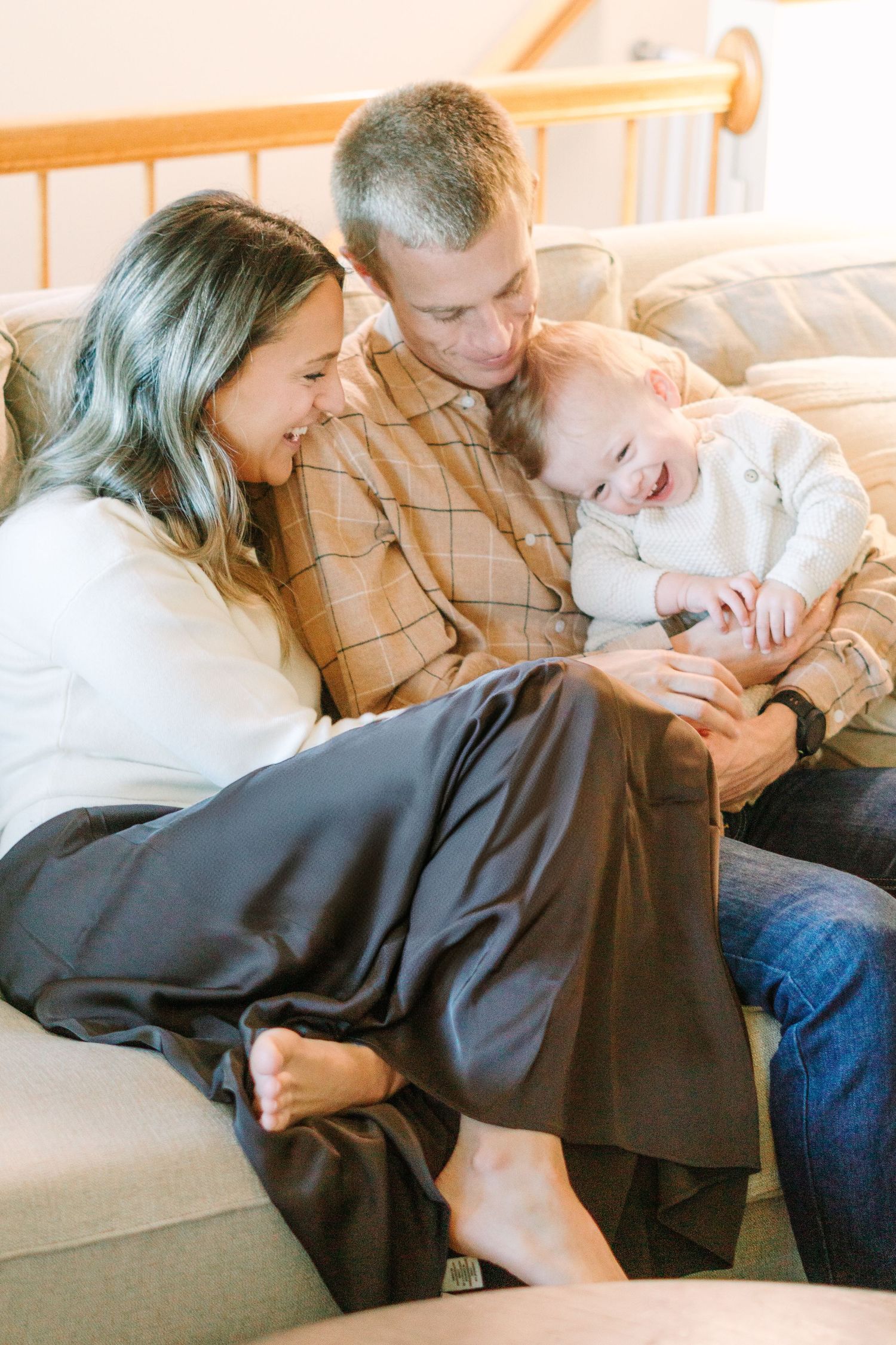 A family shares an intimate moment of laughter while relaxing on a gray couch.