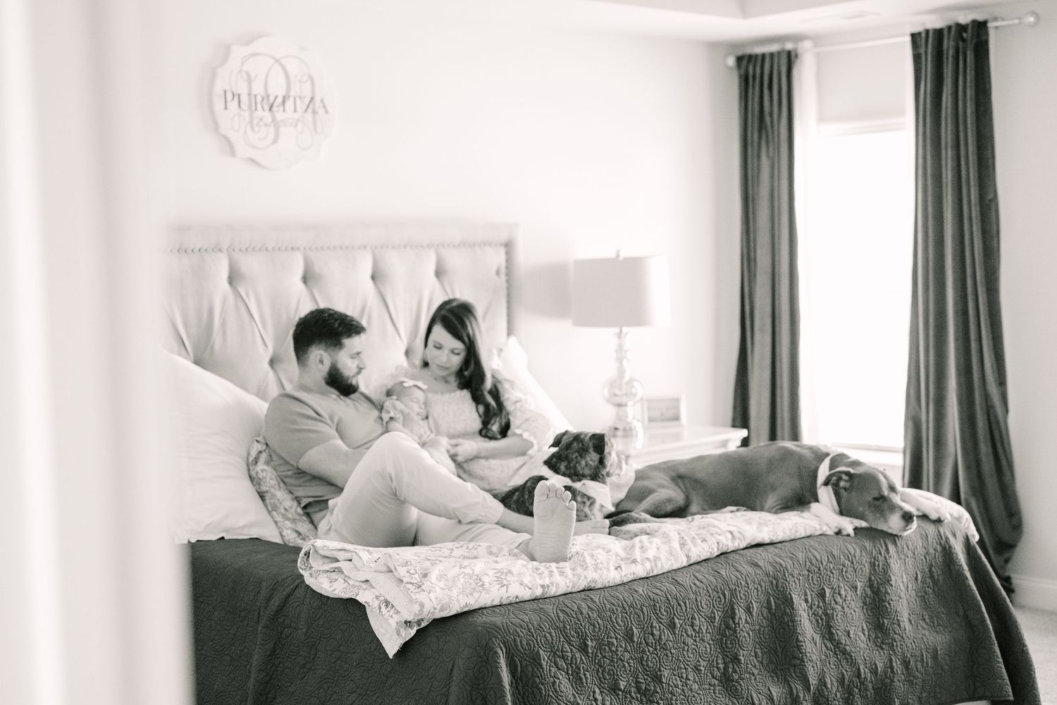 Black and white photo of cozy family moment on bed with cat relaxing together at home.
