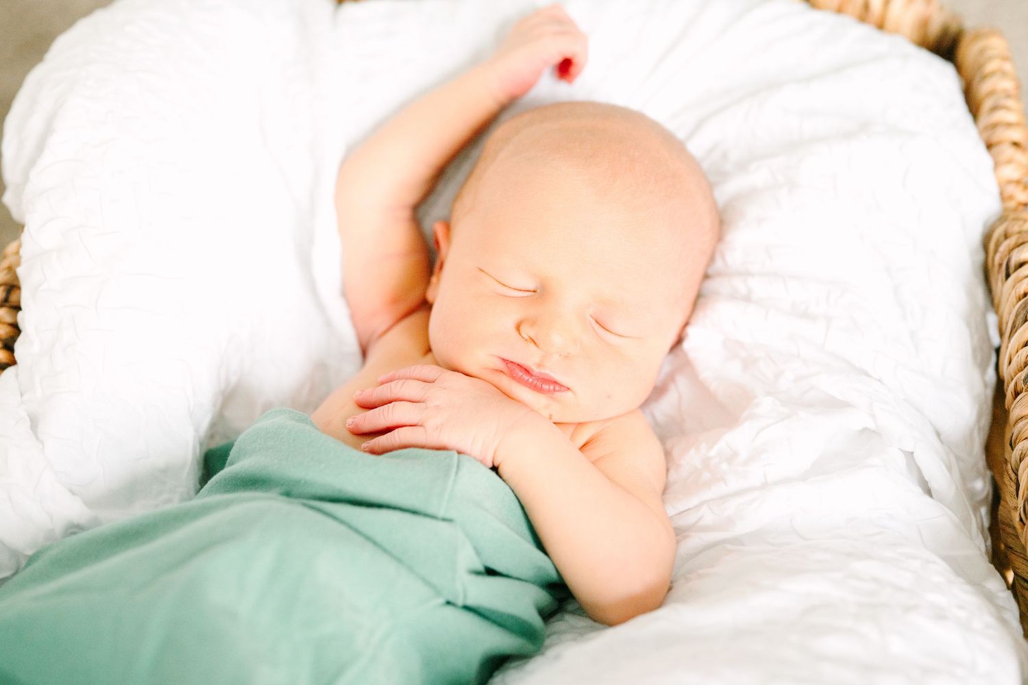 Sleeping newborn peacefully resting on white bedding in mint green swaddle wrap.