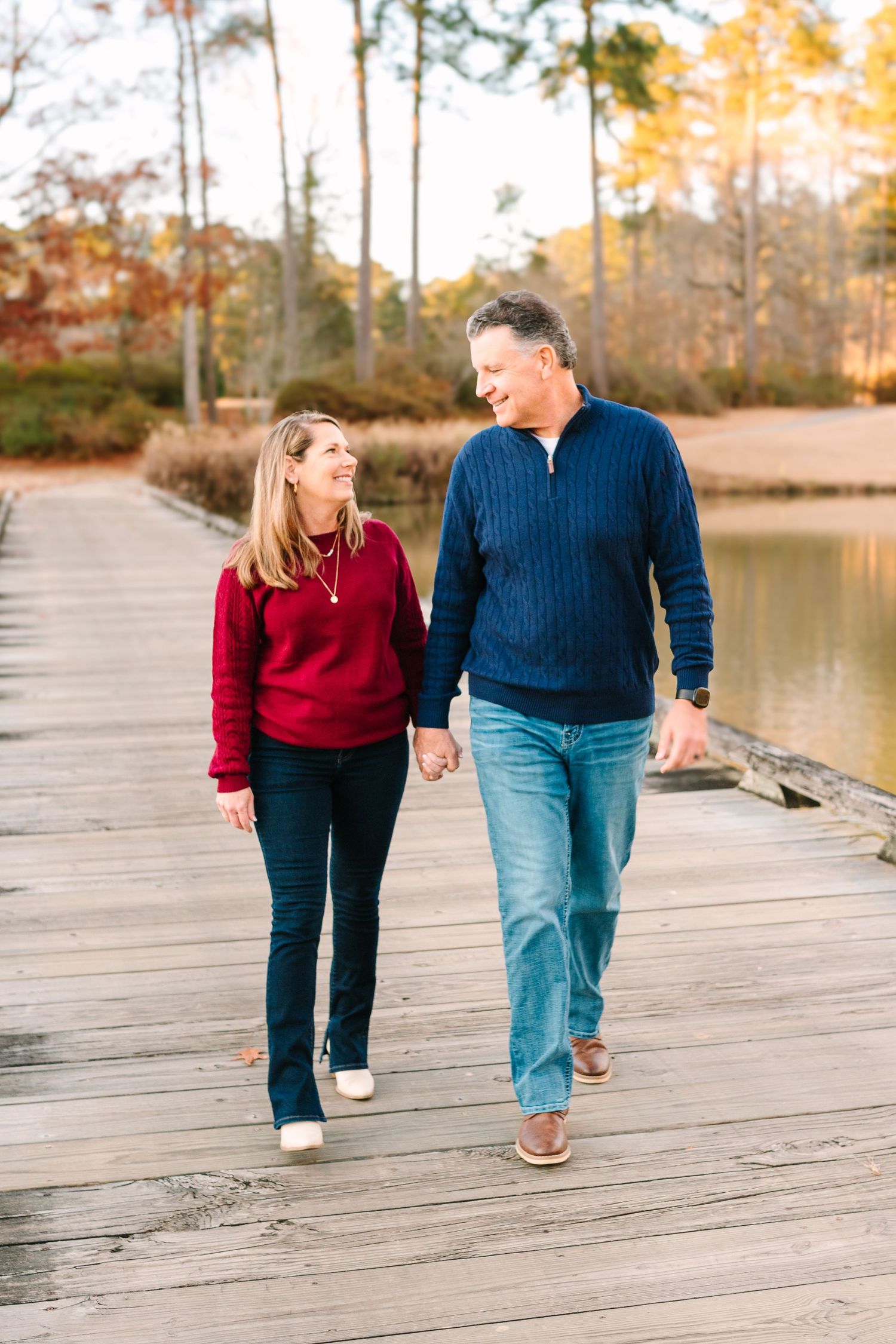 A couple strolls together on a wooden boardwalk beside a tranquil lake.