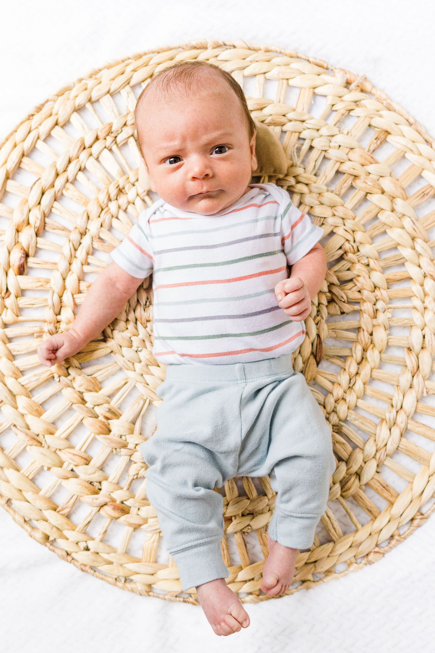 Baby in striped onesie lying on circular woven mat.