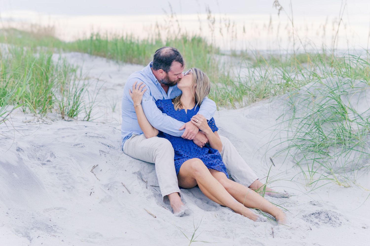 Romantic beach scene with couple sitting together in the sand among coastal dunes.