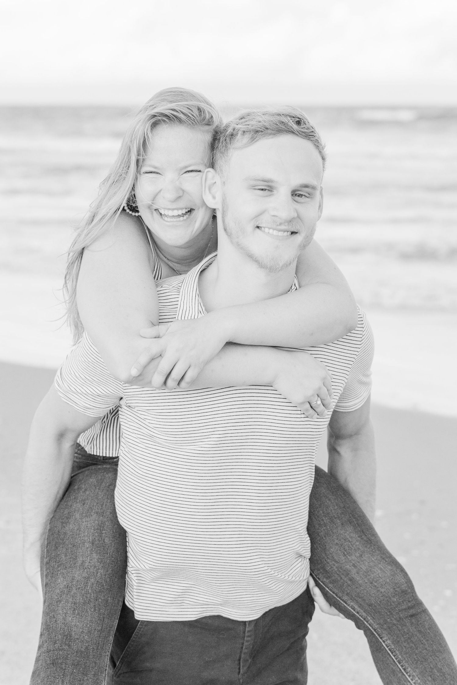 A couple shares a joyful piggyback ride moment on the beach.
