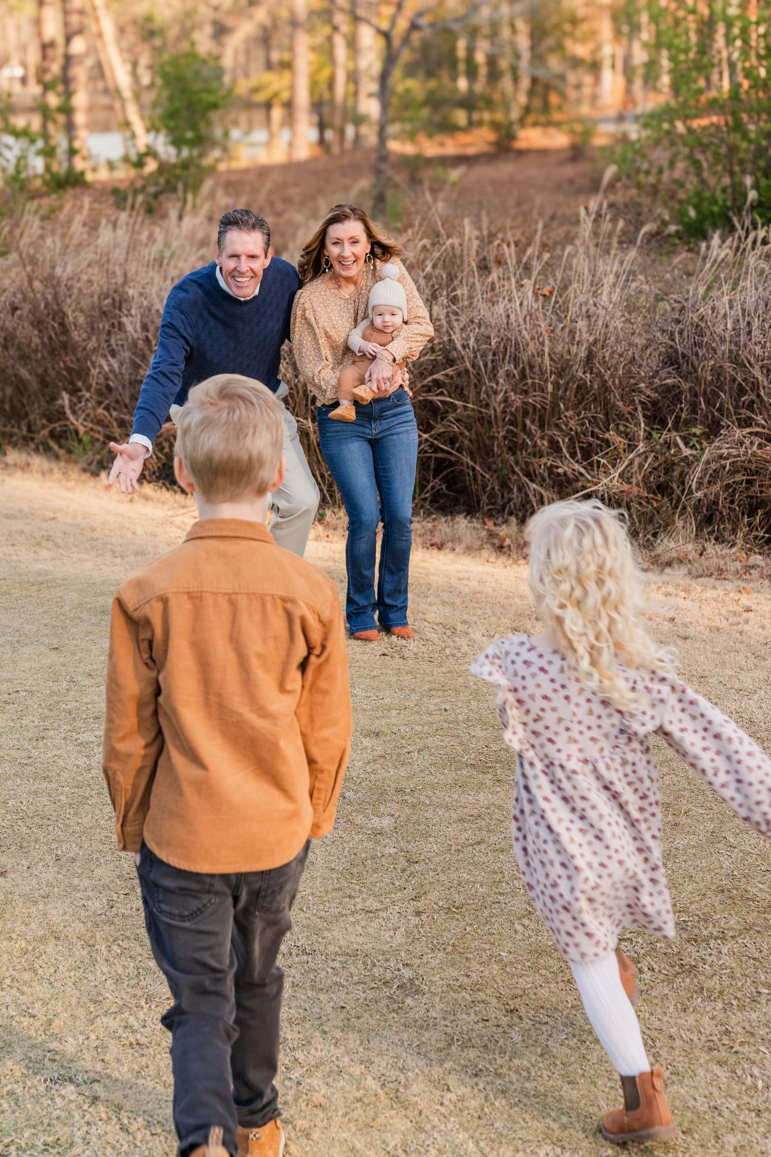 Playful family moment captured on dirt path with brush and trees in background.