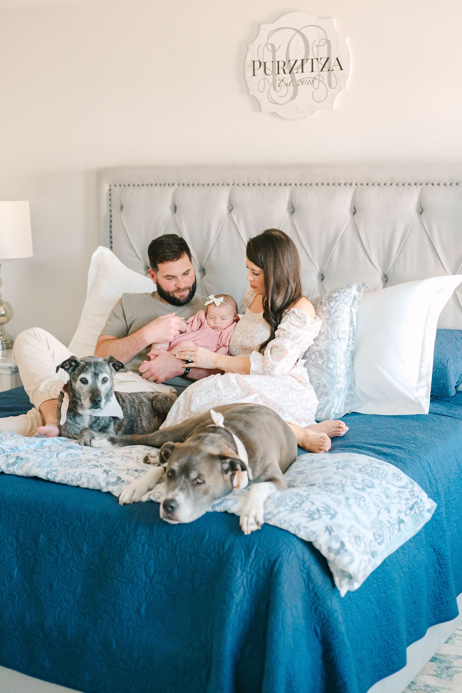 Family relaxes on bed with blue comforter alongside their two dogs while spending time together at home.