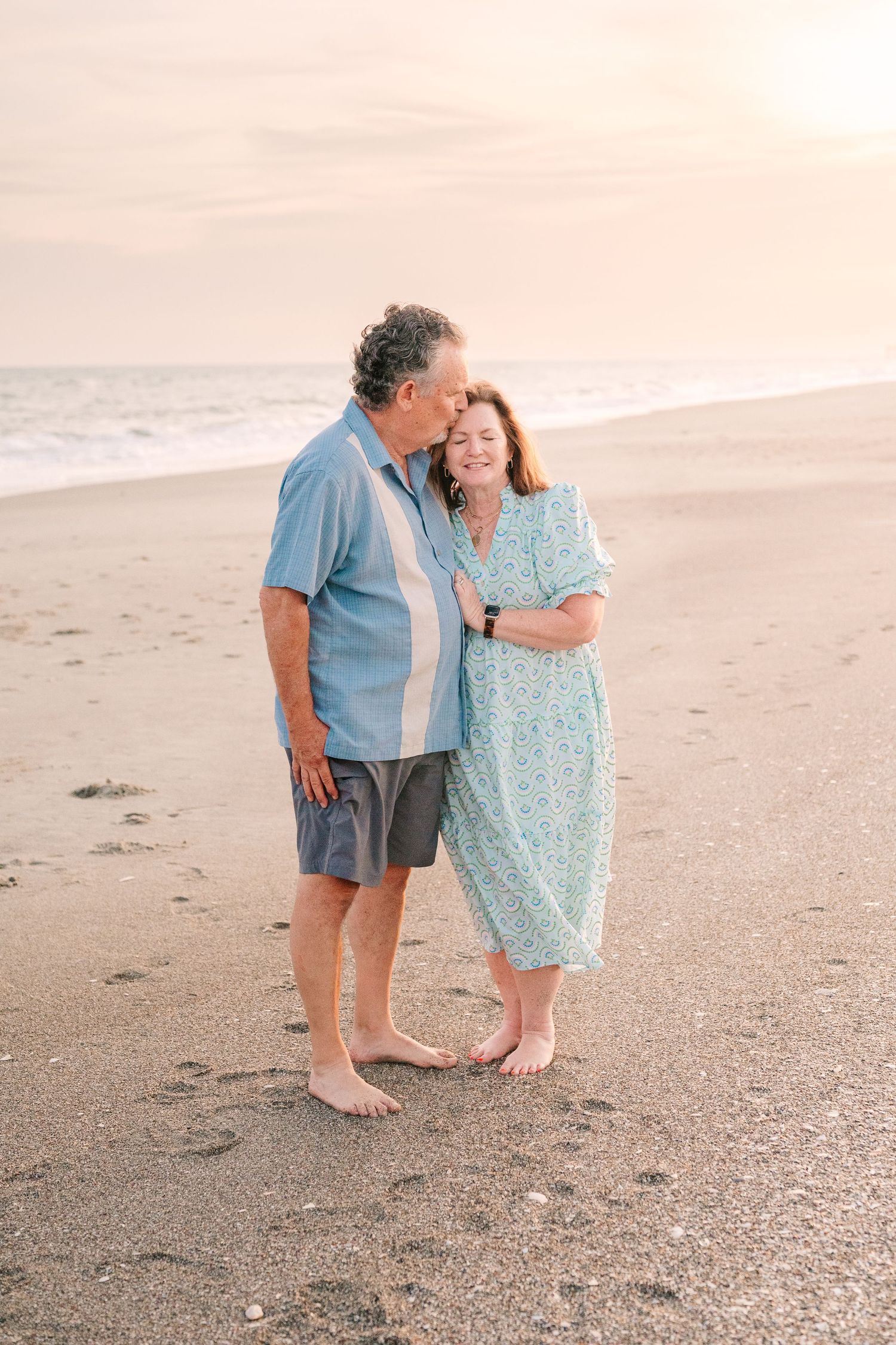 A couple shares an intimate moment while walking barefoot along a peaceful beach at sunset.