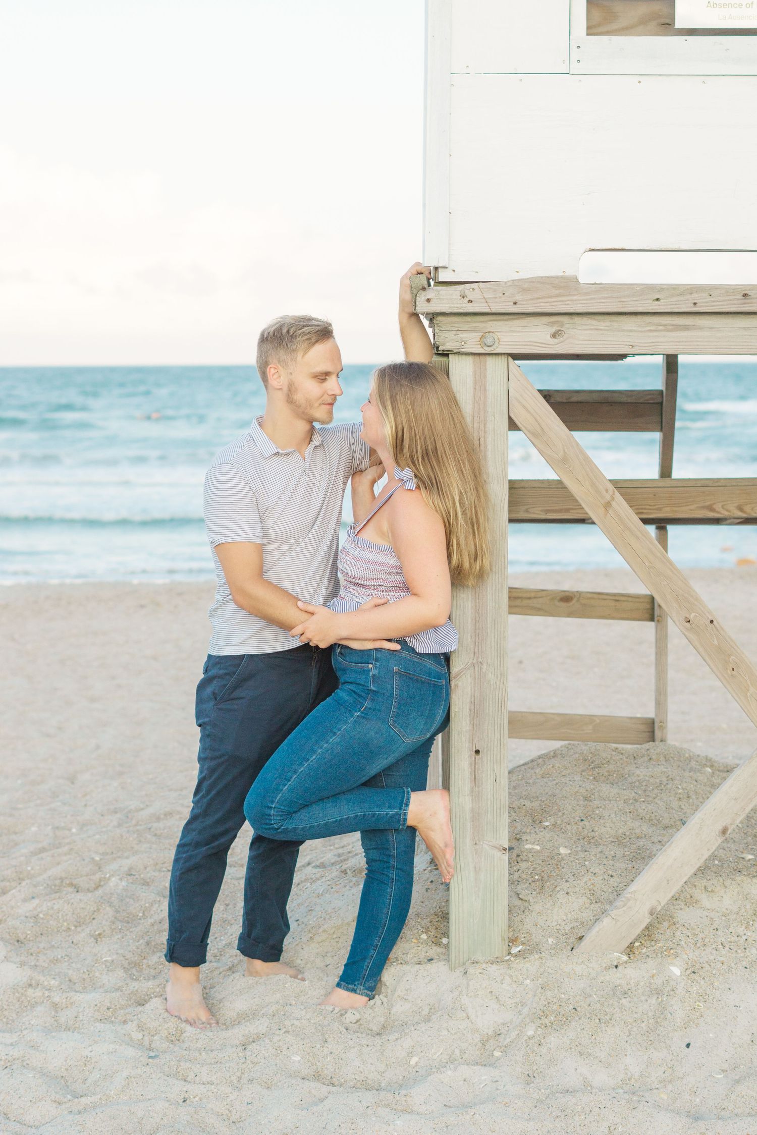 A couple shares an intimate moment by a lifeguard stand on the beach.